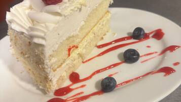 A slice of cake with whipped cream, a raspberry, and blueberries on a white plate.