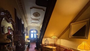 A hallway with ornate furniture, a patterned carpet, and a view into another room. - Upjohn House Inn (Kalamazoo)