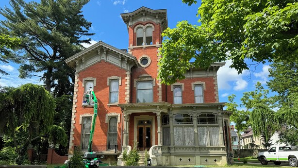 A historic red brick building with ornate white trim, a prominent tower, and a gated entrance. - Upjohn House Inn (Kalamazoo)