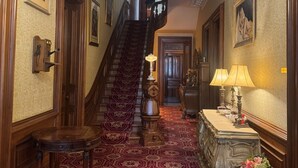 A grand hallway with a red patterned carpet, a wooden staircase, and a chandelier. - Upjohn House Inn (Kalamazoo)