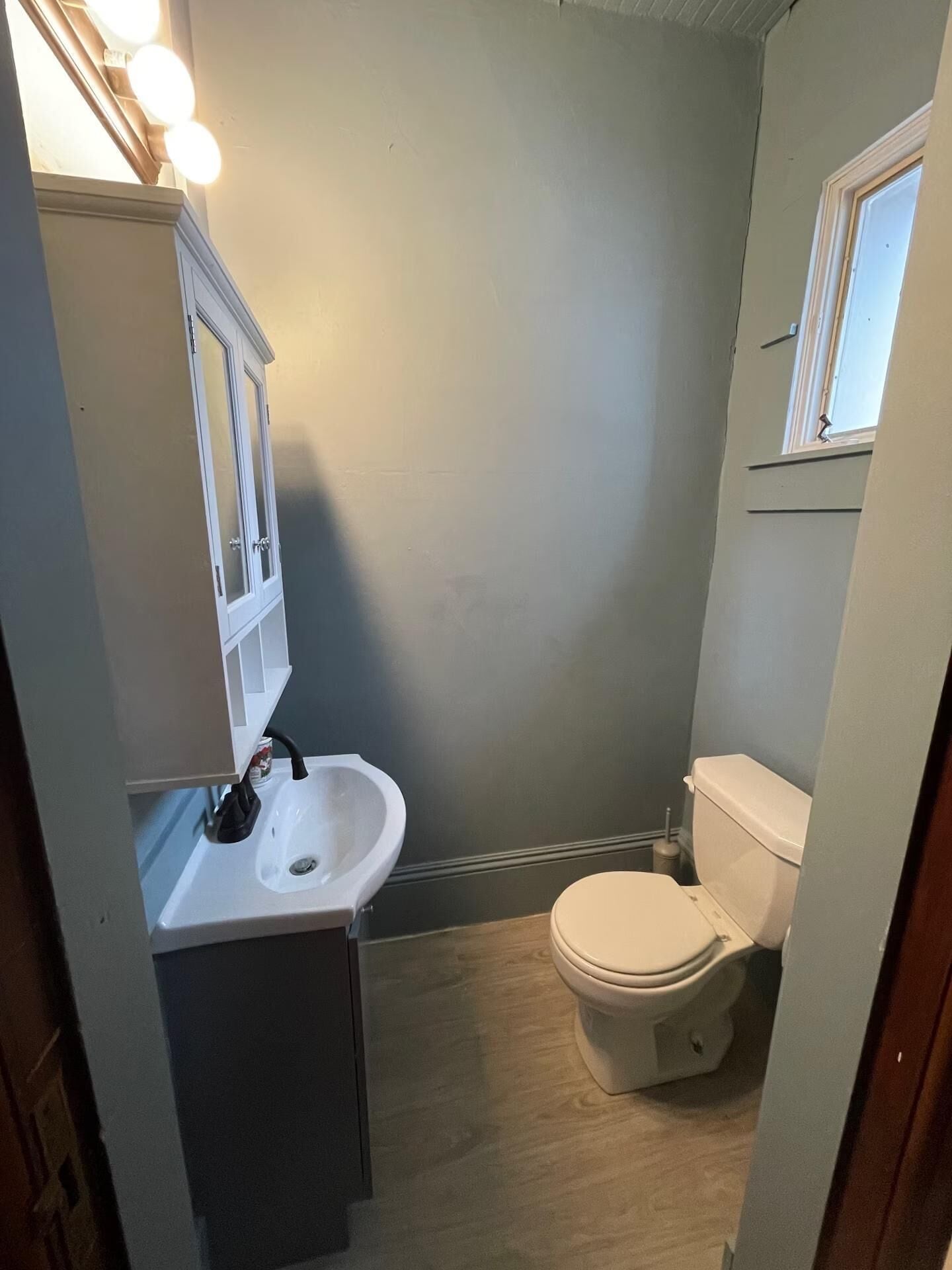 Une petite salle de bain compacte, avec un lavabo blanc, des toilettes et un meuble avec un miroir.