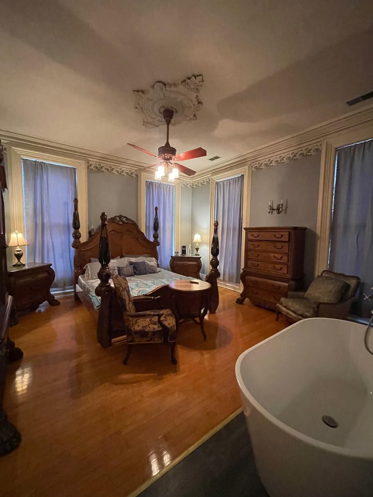 A spacious bedroom with a four-poster bed, a sitting area with a table and chairs, a large bathtub, and a wooden dresser.