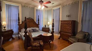 A spacious bedroom with a four-poster bed, a sitting area with a table and chairs, a large bathtub, and a wooden dresser.