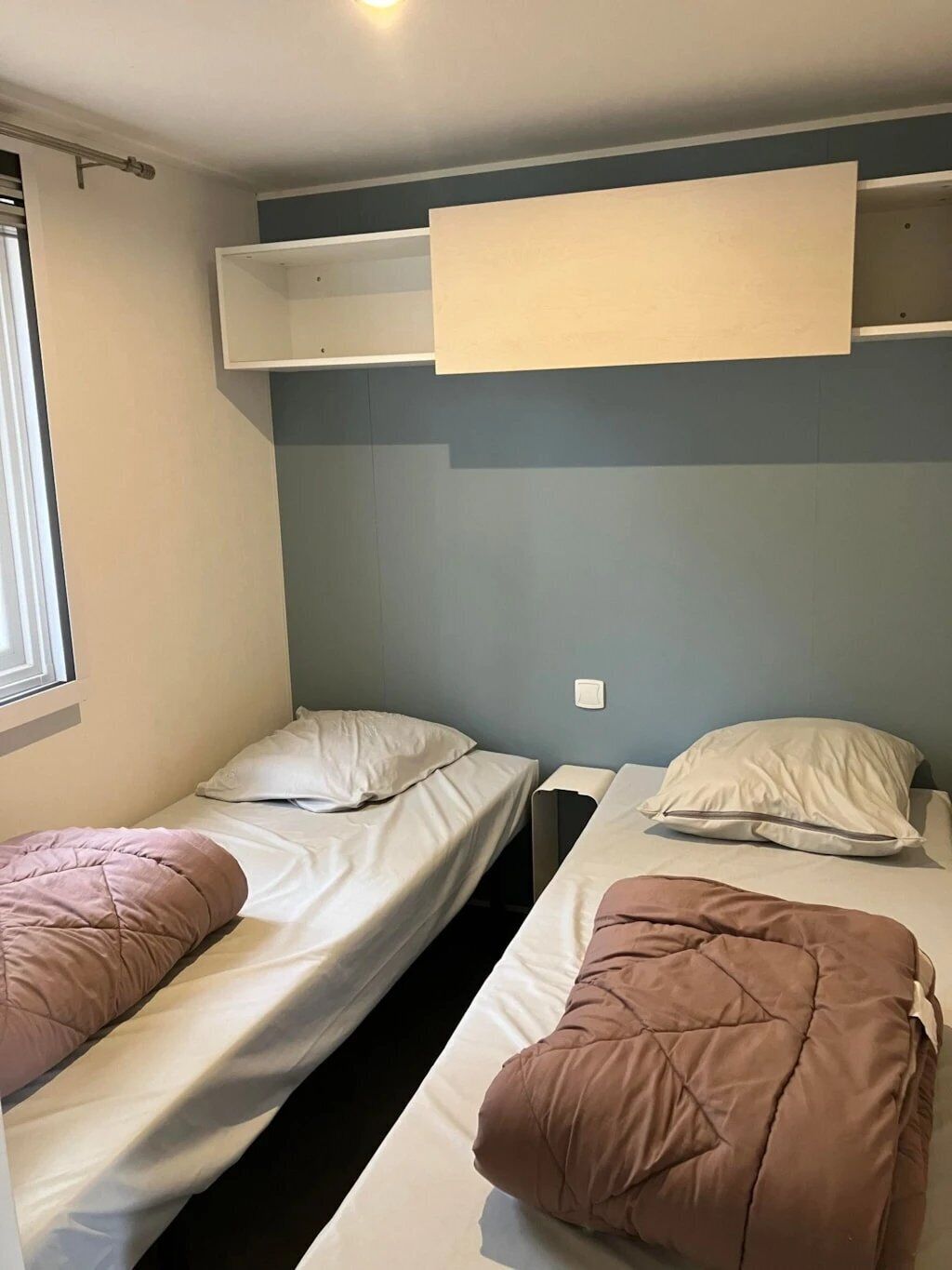 A dormitory room with two single beds, each with a pillow and a blanket.
