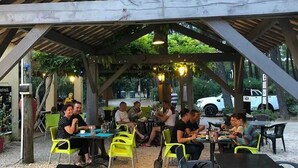 Un espace extérieur aménagé pour les repas, avec des tables et des chaises disposées sous une pergola en bois.