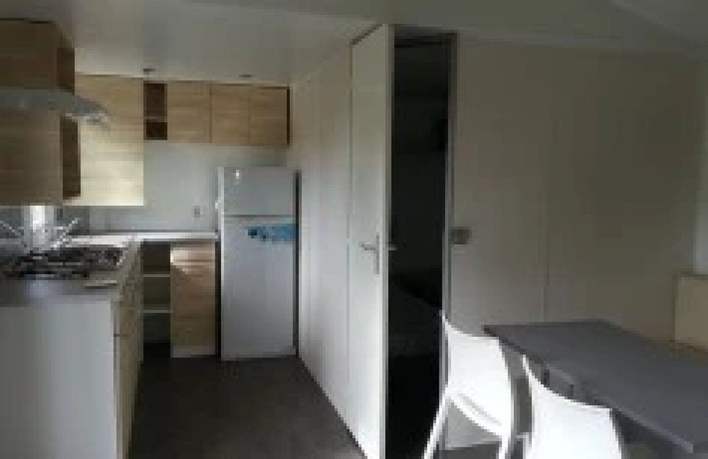 Une cuisine compacte avec des meubles en bois, un réfrigérateur et un petit coin repas agrémenté d’une chaise blanche.