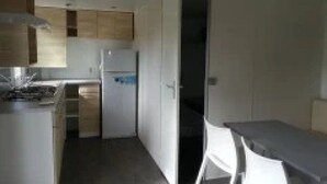 Une cuisine compacte avec des meubles en bois, un réfrigérateur et un petit coin repas agrémenté d’une chaise blanche.
