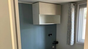 Un lit simple avec une couette rose, une tête de lit blanche et un luminaire fixé au mur.
