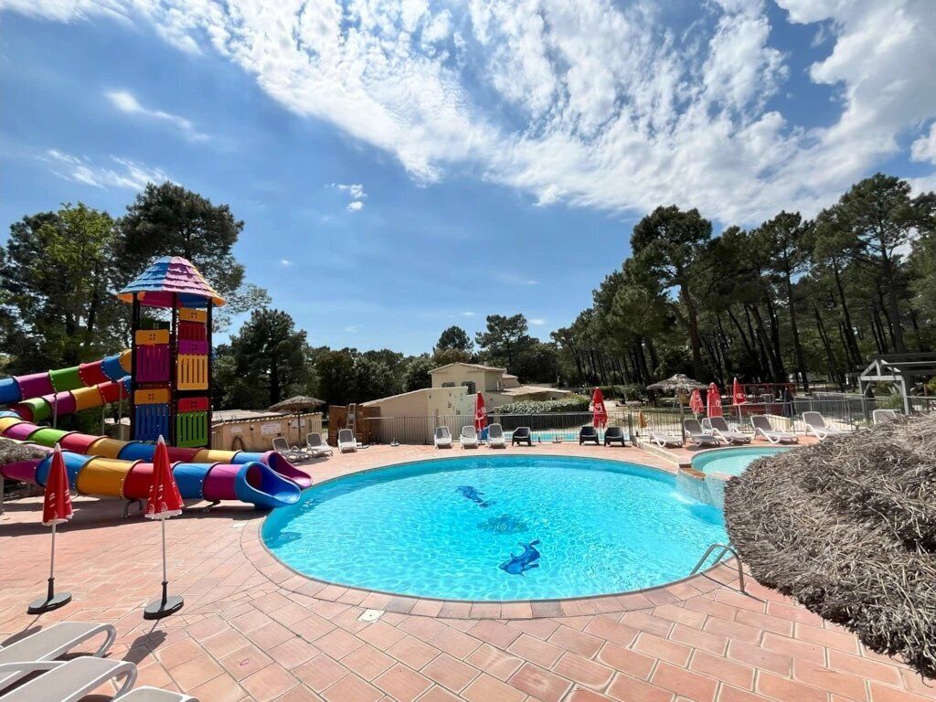 A swimming pool area with a slide, lounge chairs, and umbrellas.