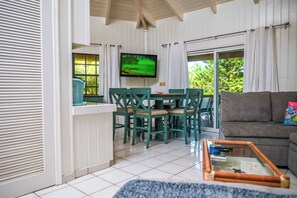 A room with a dining area, a TV mounted on the wall, a sofa, and a glass coffee table.