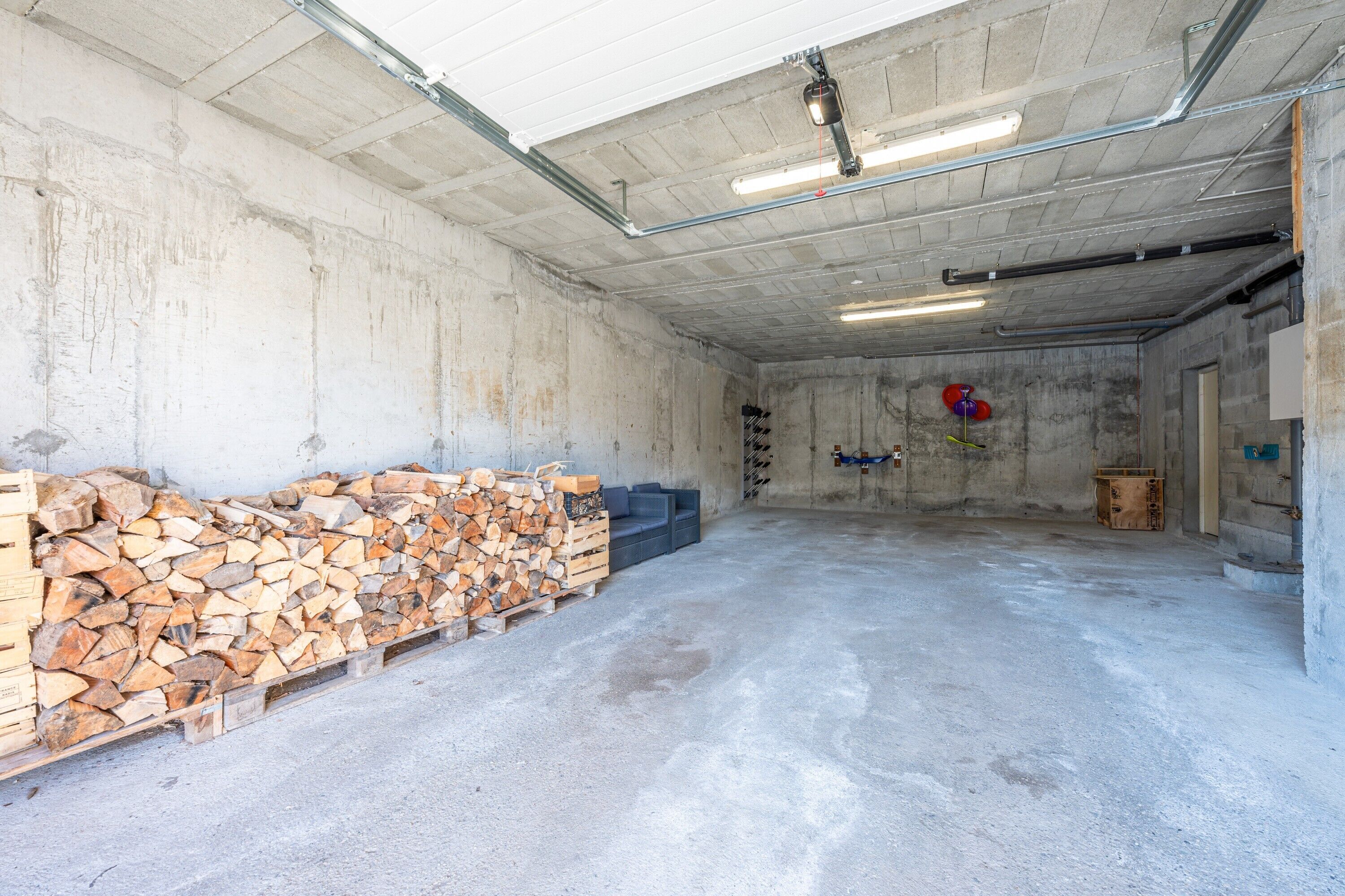 Un vaste espace intérieur aux murs et au plafond en béton, comprenant une pile de bois de chauffage, un canapé bleu et un ballon rouge.
