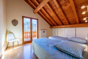 Slaapkamer met houten balken, een bed, een stoel en een uitzicht door een deur.