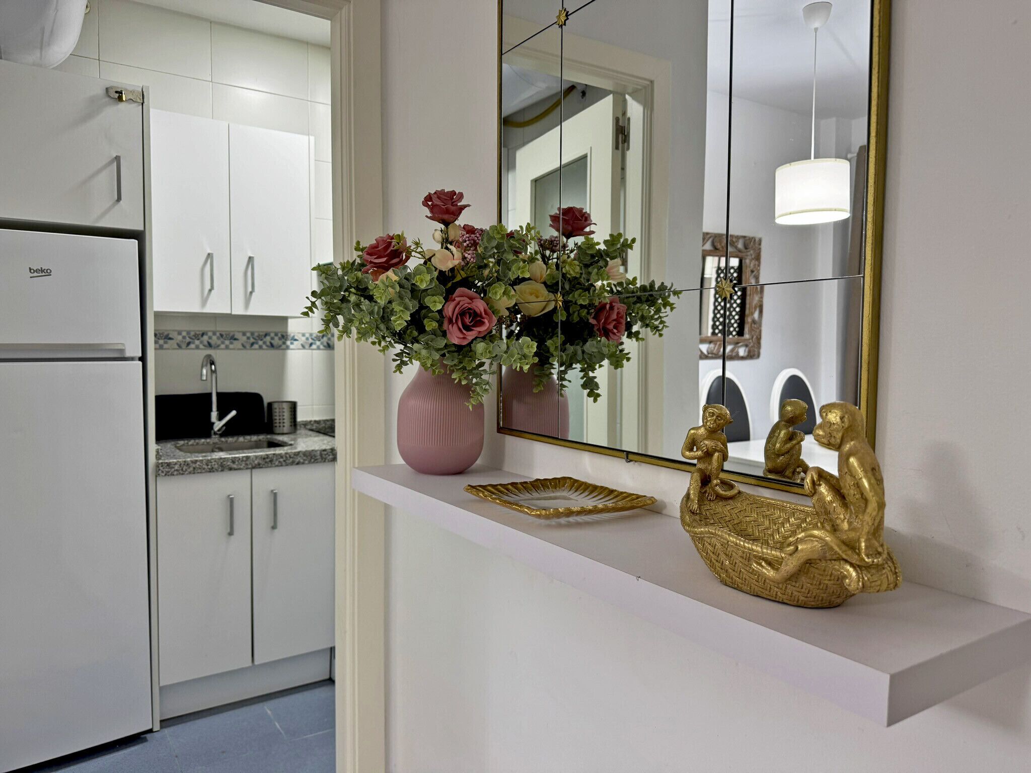 Een keuken met witte kastjes, een roze vaas met bloemen en een gouden decoratie op het aanrecht.