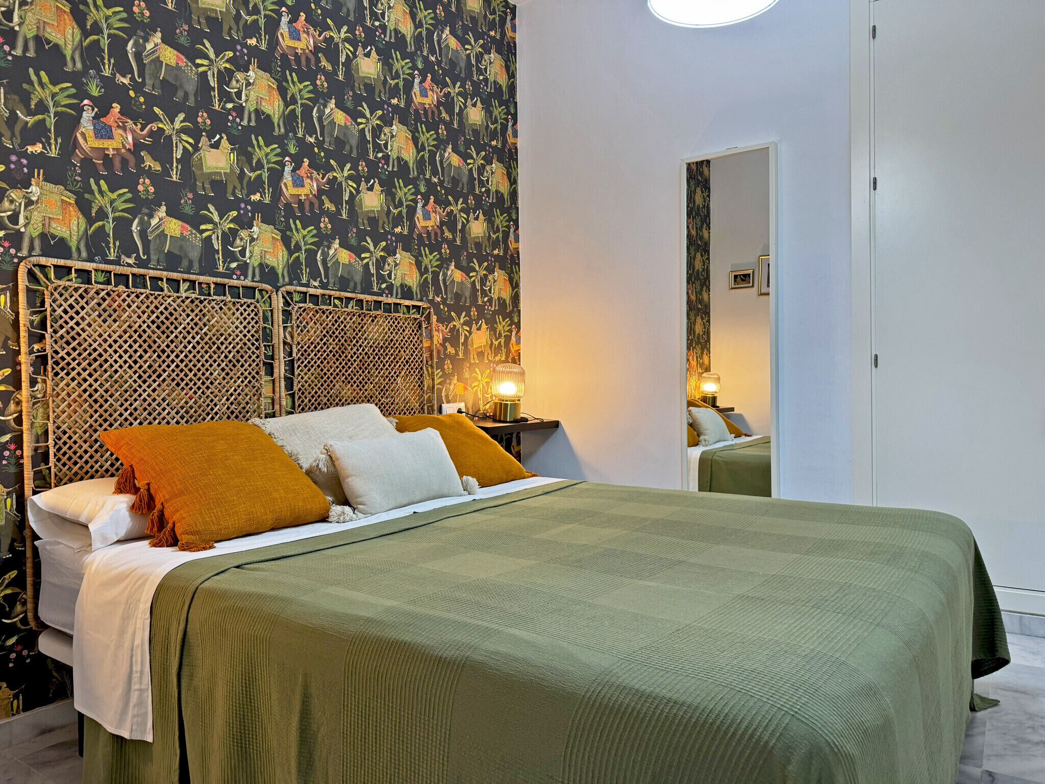 Een hotelkamer met een bed, een geweven hoofdbord en een muurschildering van olifanten.