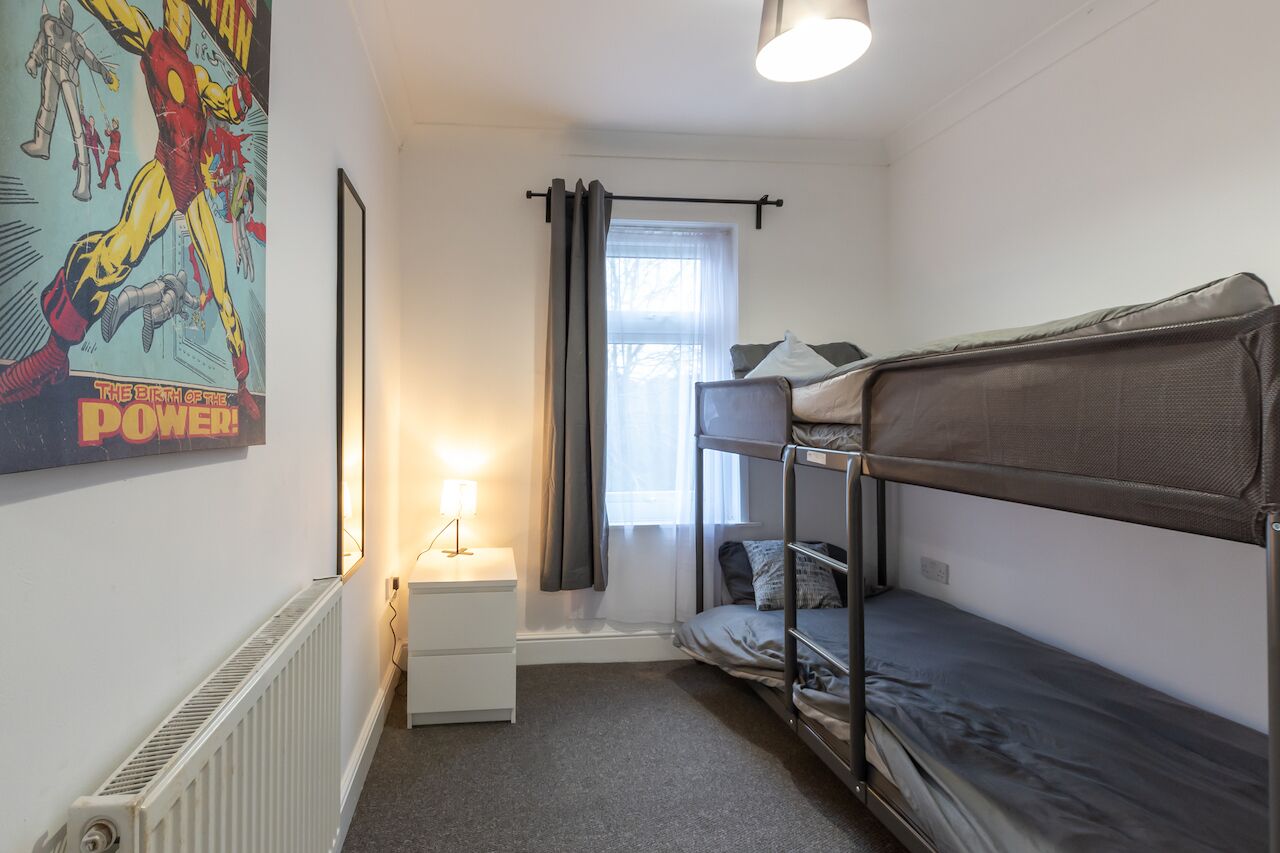 A small, compact room with bunk beds, a bedside table, a radiator, and a poster on the wall.