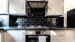 A modern kitchen with black tiled backsplash, stainless steel appliances, and white cabinetry.
