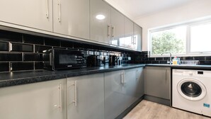 A modern kitchen with grey cabinets, a black countertop, and a built-in washing machine.