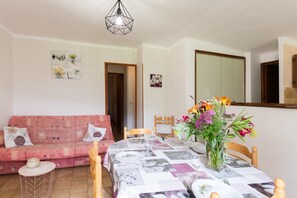 Een eetgedeelte met een tafel gedekt voor twee personen, een roze bank en een spiegel aan de muur.