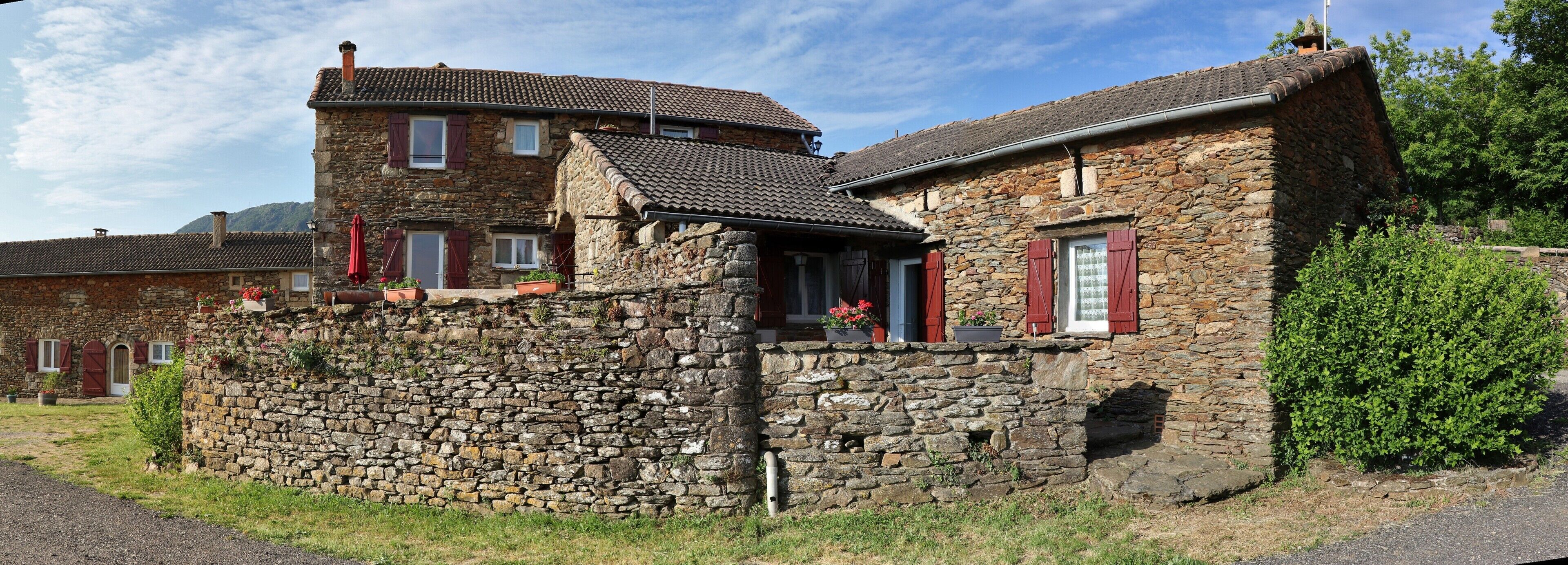 Un bâtiment en pierre avec un toit en tuiles, un petit balcon doté de volets rouges et un mur en pierre.