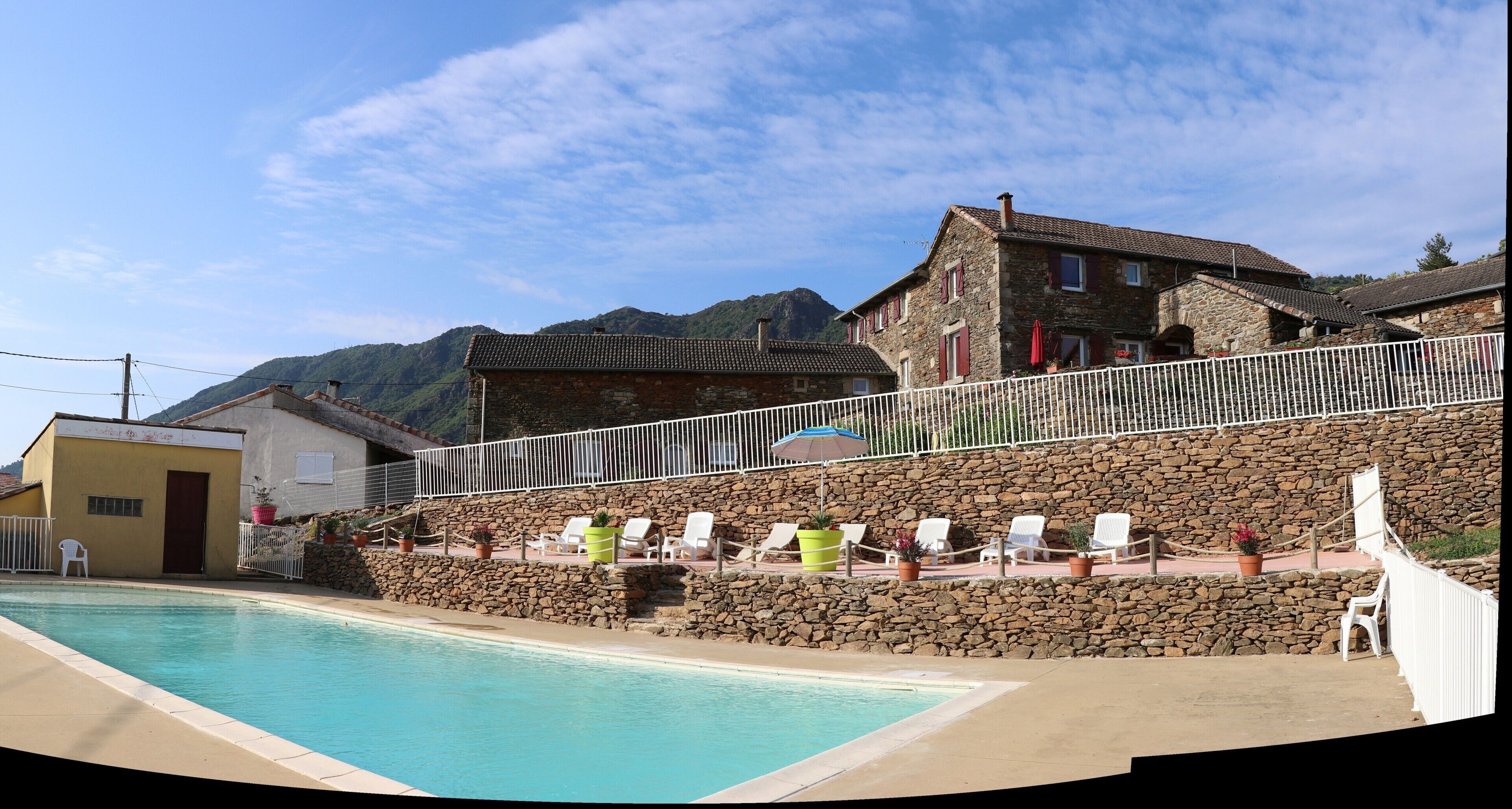 A pool area with lounge chairs, a stone wall, and a building with a tiled roof.