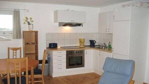 A compact kitchen with a built-in oven, a coffee maker, and a sink. There is a dining table with chairs and a blue chair in the foreground. - Hausboot in Kroeslin am Bodden (Kröslin)