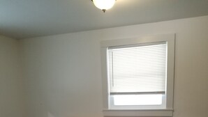 A bedroom with a single bed, a nightstand, a lamp, and a window with blinds. - The Chicken Coop (Staatsburg)