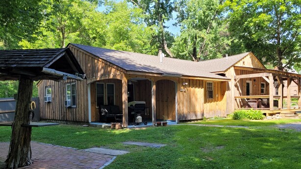 Eine Holzhütte mit Veranda, Grill und Baum im Vordergrund.