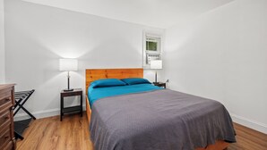 A bedroom with a bed, two bedside tables, a lamp, a dresser, and a window with blinds. - The Chicken Coop (Staatsburg)