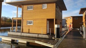 A wooden cabin with a dock extending into a body of water, featuring a balcony and a small window. - Hausboot in Kroeslin am Bodden (Kröslin)
