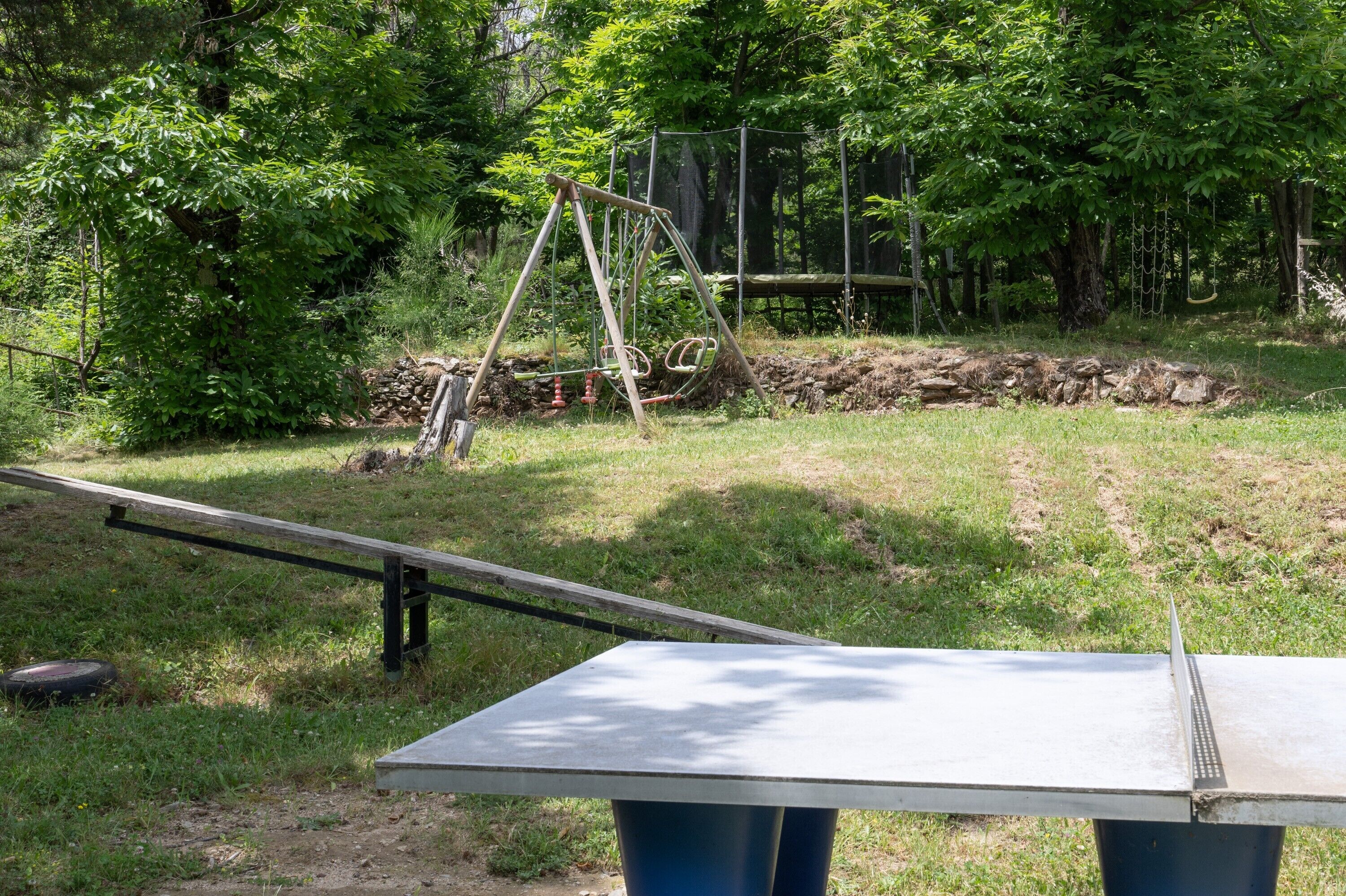 Une table de ping-pong installée dans un espace extérieur, avec une balançoire et des arbres en arrière-plan.