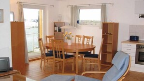 A dining area with a wooden table and chairs, a small kitchen with a stove, and a view of the sea through large windows. - Hausboot in Kroeslin am Bodden (Kröslin)