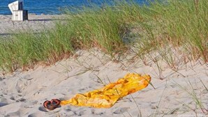 A beach scene with a yellow towel and sandals on the sand, a chair, and grass in the background. - Hausboot in Barth am Barther Bodden (Barth)