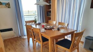 A dining area with a wooden table and chairs, a bookshelf, and a view of the sea through large windows. - Hausboot in Barth am Barther Bodden (Barth)