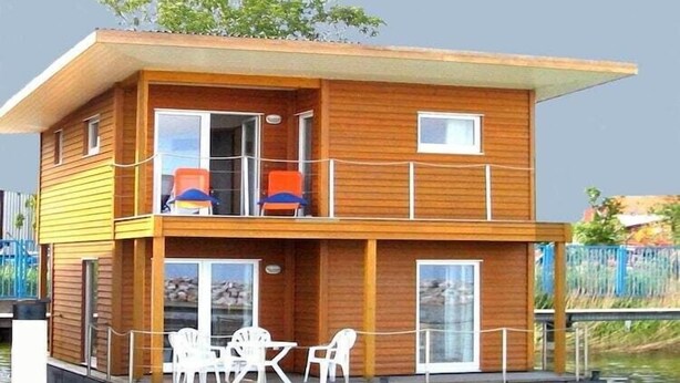 A two-story wooden houseboat with a balcony, outdoor seating, and a dock. - Hausboot in Barth am Barther Bodden (Barth)