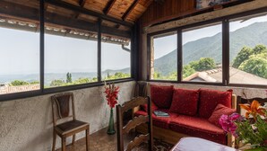 A room with a wooden ceiling, a red sofa, a wooden chair, and a view of mountains through large windows. - Holiday Home 'Le Pigeonnier' with Mountain View, Shared Pool and Air Conditioning (Gravières)