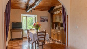 A dining area with a table set for two, a television on a stand, and a view of the outdoors through a window. - Holiday Home 'Le Pigeonnier' with Mountain View, Shared Pool and Air Conditioning (Gravières)