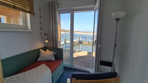 A room with a bed, a chair, a lamp, and a view of a dock and water. - Hausboot in Barth am Barther Bodden (Barth)