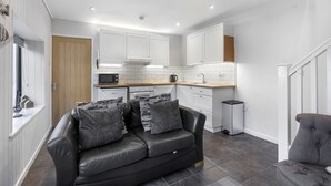 Cocina moderna con armarios blancos, un sofá de cuero negro y un sillón gris.