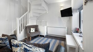 Una sala de estar moderna con una escalera, un sillón gris, un escritorio blanco y un televisor de pantalla plana.