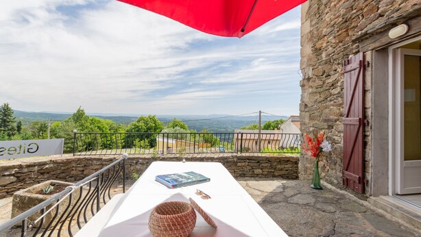 A terrace with a stone wall, a red umbrella, a book, a pair of glasses, and a vase with flowers.