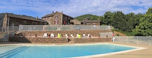 Un bâtiment en pierre avec une piscine, des chaises blanches et une clôture blanche.