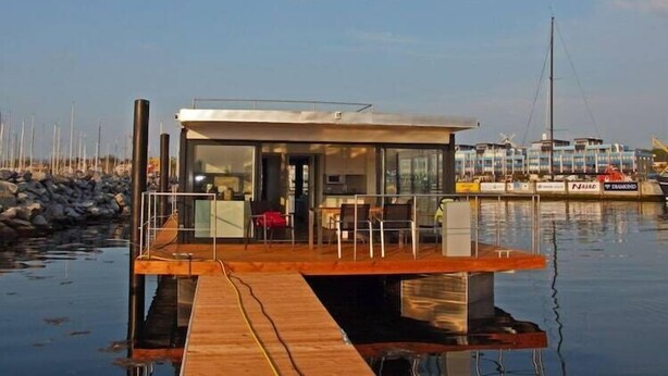A floating structure with a wooden deck, glass walls, and a small seating area. - Hausboot in Laboe an der Kieler Foerde (Laboe)