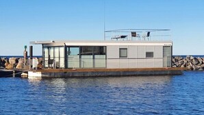A modern floating house with a glass facade, a deck, and a small outdoor seating area. - Hausboot in Laboe an der Kieler Foerde (Laboe)