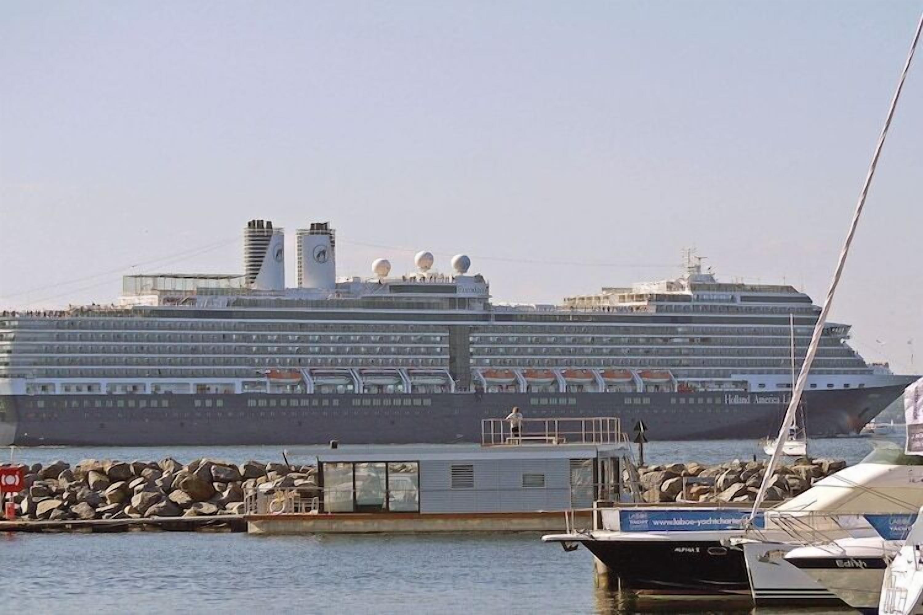 A large cruise ship docked at a port with a small boat in the foreground.