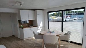 A modern kitchen with white cabinets, a microwave, and a dining area with a round table and four chairs. - Hausboot in Laboe an der Kieler Foerde (Laboe)