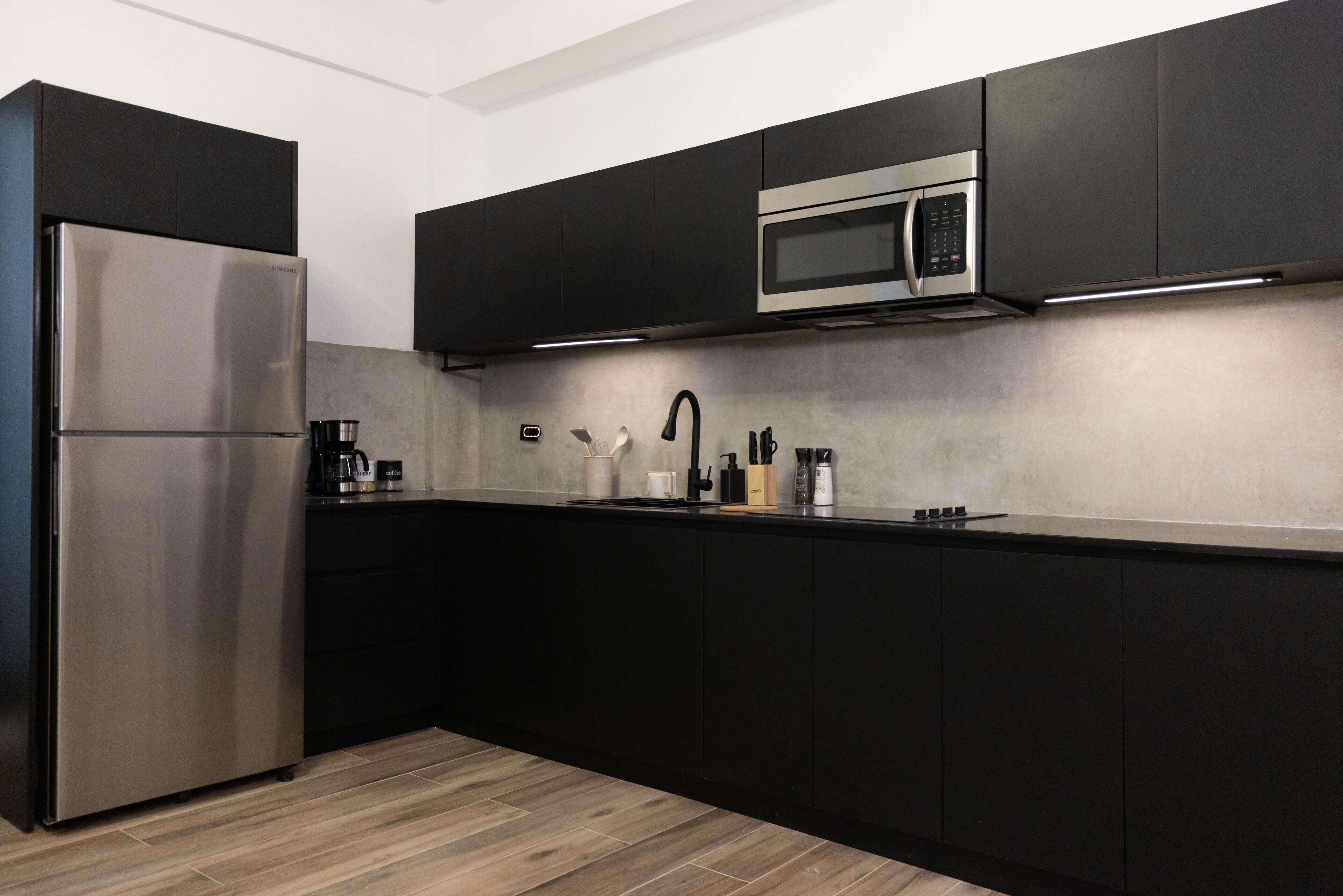 A modern kitchen with black cabinets, stainless steel appliances, and a wooden floor.