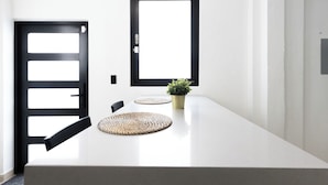 Ein modernes Interieur mit einem weißen Tisch, zwei Fenstern mit schwarzem Rahmen und einem Blumentopf.