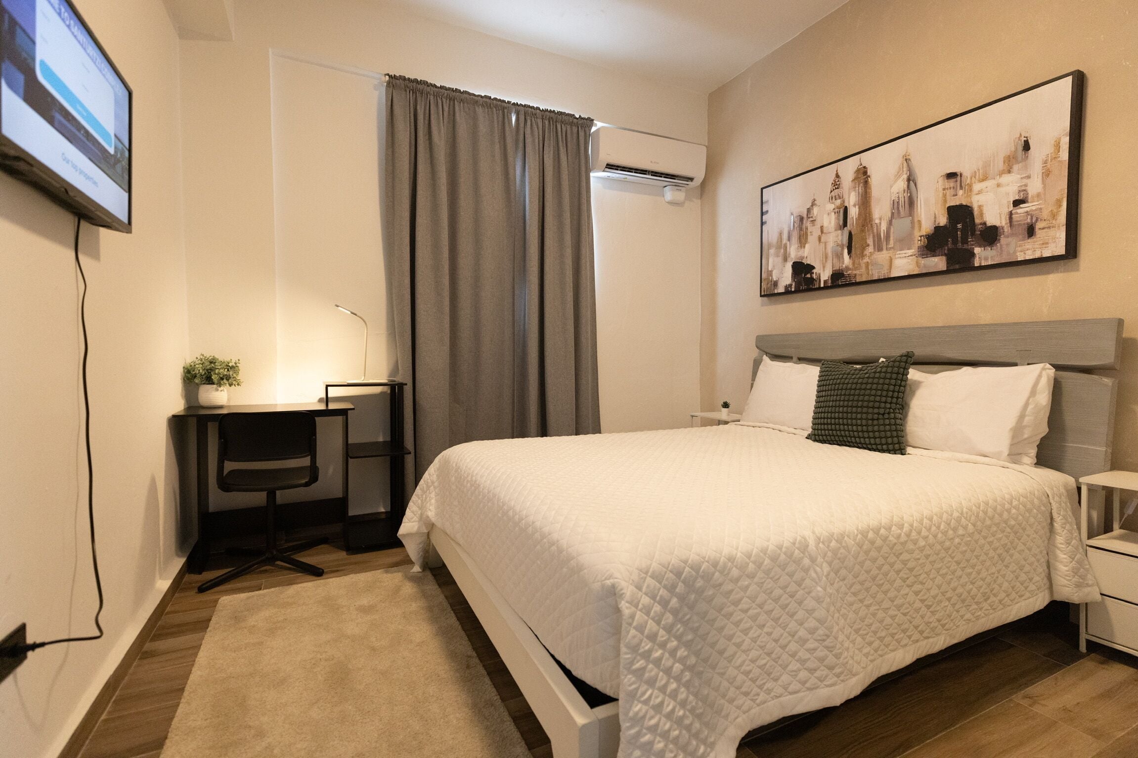 Una habitación de hotel moderna con una cama grande, un escritorio con una silla, una mesita y un aire acondicionado instalado en la pared.