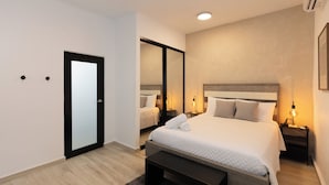 Ein modernes Hotelzimmer mit einem großen Bett, einem Nachttisch mit Lampe, einem Kleiderschrank und einer Bank.