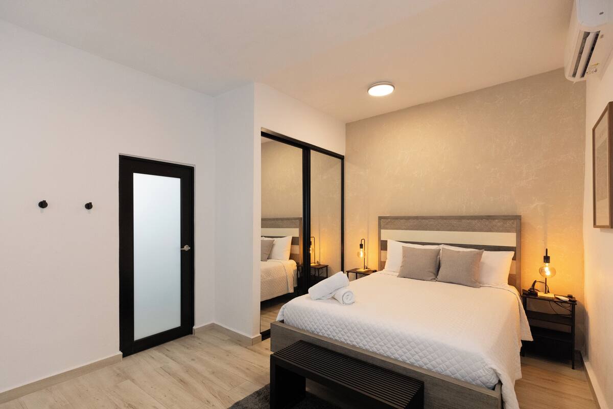 Une chambre d’hôtel moderne avec un grand lit, une table de chevet avec une lampe, une armoire et un banc.